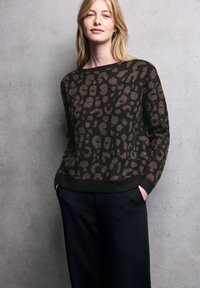 Maglione a motivo leopardato marrone e nero realizzato in morbido tessuto a maglia, con scollo rotondo e polsini a costine, abbinato a pantaloni scuri.