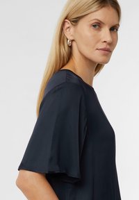 Granatowa bluzka o luźnym kroju, z krótkimi, rozszerzającymi się rękawami i okrągłym dekoltem, wykonana z gładkiego materiału o delikatnym połysku.