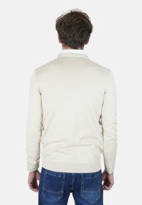Maglione beige in tessuto morbido, con texture liscia, design aderente e polsini a coste, abbinato a jeans di denim blu.