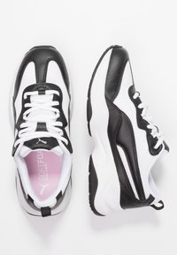 Musta-valkoiset urheilutennarit, joissa on teksturoitu nahkainen ja verkkokangas päällinen, nauhallinen kiinnitys, pehmustettu kaulus ja paksu kumipohja.