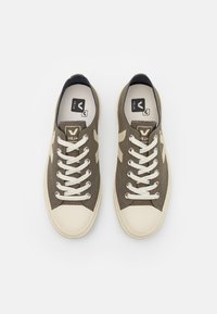 Brune canvas joggesko med kremfargede gummisåler, med teksturert overflate, hvite snørebånd og brune detaljer på siden.