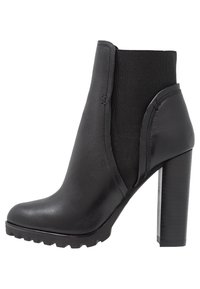 Bottine noire en cuir avec des panneaux latéraux élastiques. Elle dispose d'un talon haut chunky et d'une semelle en caoutchouc texturé avec un motif à crampons.
