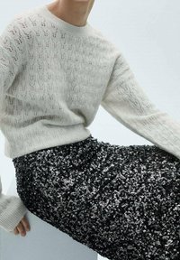 Jasnoszary sweter z dzianiny o fakturowanym wzorze i długich rękawach, połączony z czarną cekinową spódnicą, tworzący kontrast faktur.