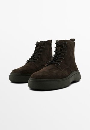 Braune Wildleder-Stiefeletten mit strukturierter Oberfläche, runder Spitze, schwarzen Schnürsenkeln und einer dicken, dunklen Gummisohle. Reißverschlussdetail an der Seite.