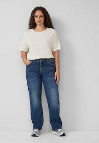 Cremefarbiges T-Shirt mit kurzen Ärmeln, kombiniert mit gerade geschnittenen Jeans in mittlerem Waschmittel und grauen Sneakers. Einfaches Design mit lockerer Passform.