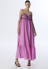 Roze maxi-jurk met spaghettistringen, voorzien van zwarte geborduurde details op de bustier en een gerimpelde zoom. Lichtgewicht stof.