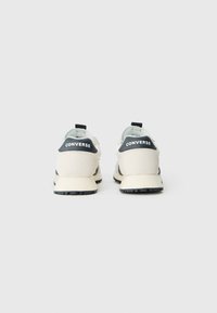 Des chaussures de sport blanches et grises avec des semelles noires, dotées d'un col rembourré, d'une tige en mesh et du logo "CONVERSE" sur le talon.