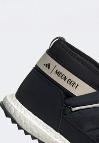Černé Moon Boot s hladkým textilním svrškem, metalickým stříbrným akcentem a texturovanou bílou podrážkou, vybavené bezpečným systémem šněrování a detailem loga.