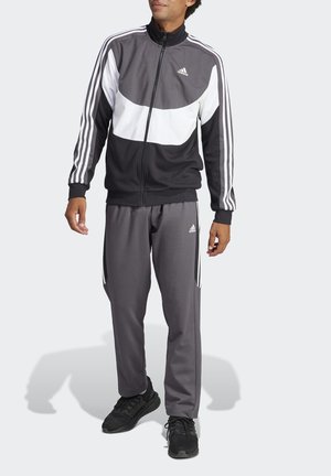 Tuta sportiva nera e grigia con giacca con zip e dettagli bianchi, tre strisce bianche sulle maniche e pantaloni abbinati.