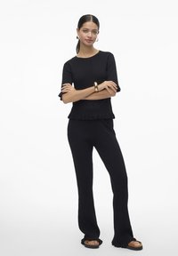 Ensemble noir à deux pièces comprenant un haut à manches courtes côtelé avec un ourlet volanté et un pantalon évasé assorti. Le matériau est doux et texturé.