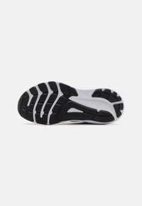Semelle de chaussure en caoutchouc noir texturé, avec un intermédiaire blanc, un design incurvé et des rainures définies pour la traction et l'adhérence.