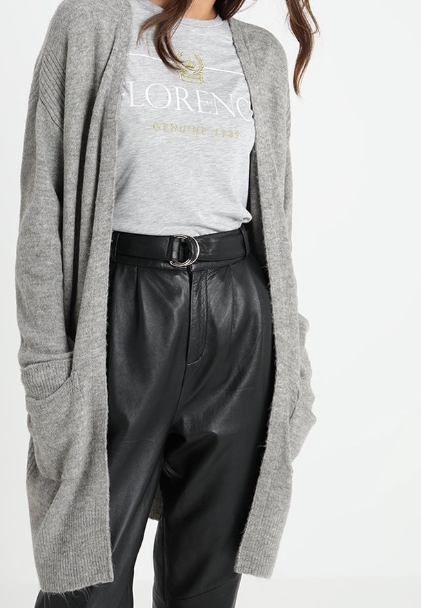 Grå stickad kofta med öppen fram, ribbade detaljer och sidofickor, bärs över en ljusgrå t-shirt och svarta läderbyxor.