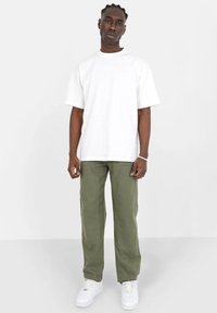 Hvid bomulds T-shirt med rund hals, parret med grønne cargo bukser med frontlommer og lige ben design, afsluttet med hvide sneakers.