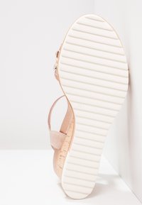 Sandale en suede rose clair avec une semelle plate en caoutchouc blanc, dotée d'une surface texturée et d'une sangle ajustable pour la cheville.
