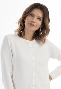 Cardigan bianco con scollatura rotonda, maniche lunghe e chiusura con bottoni. Realizzato in un tessuto morbido e testurizzato.