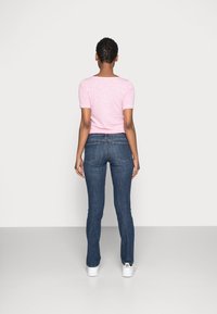 Top de manga corta rosa con escote redondo, combinado con jeans ajustados azul oscuro con detalles en los bolsillos, y zapatillas blancas.