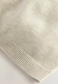 Tissu en tricot beige avec une texture lisse et un ourlet côtelé, présentant un design simple et épuré ainsi que des variations subtiles dans la couleur du fil.