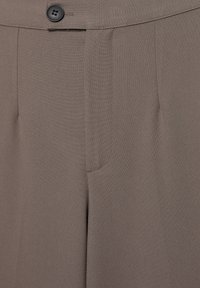 Bruine op maat gemaakte broek gemaakt van een soepele stof, met voorplooien en een enkele zwarte knoop op de tailleband.