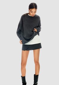 Maglione grigio scuro oversize in maglia, indossato sopra una maglietta bianca, abbinato a una gonna nera a righe e stivali neri fino al ginocchio.