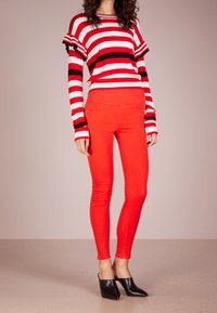 Jean skinny rouge assorti à un haut à manches longues rouge et blanc rayé avec des manches à volants. Des mules noires à bout pointu complètent la tenue.