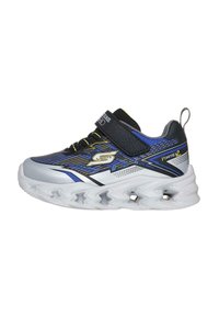 Zapatillas deportivas con un upper sintético en negro, azul y plata, que cuentan con una correa de Velcro, detalles texturizados y una suela blanca con patrón de ondas.