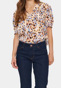 Top à manches courtes en crème clair avec un motif léopard coloré. Associé à un jean en denim bleu foncé au style classique.