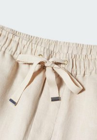 Pantalon en tissu beige avec taille élastique et cordon noué avec embouts métalliques et détails cousus.