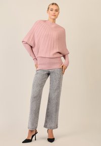 Rosa geripptes oversized Sweatshirt mit hohem Kragen, kombiniert mit grauen weit geschnittenen Jeans mit gepunktetem Muster und schwarzen High Heels.