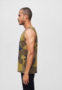 Tank topp i kamuflasjemønster med nyanser av grønn, gul og blå. Stoffet ser mykt ut, har brede armhulser og en avslappet passform.