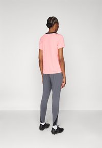Treningstøy med en lys rosa t-skjorte med korte ermer og grå tapered bukser med svarte sideakenter. Svarte joggesko fullfører antrekket.