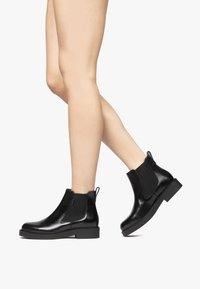 Black leather Chelsea boots with elastic side panels, rounded toe, and flat sole. Features a pull tab for easy wear. Smooth texture.