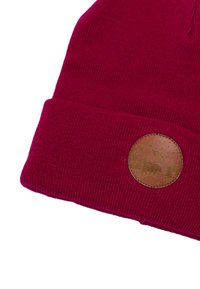 Bordowa dzianinowa czapka z podwiniętym brzegiem, z okrągłą naszywką z materiału przypominającego skórę, na której wytłoczono wzór z niedźwiedziem i sosnami. Gładka faktura.