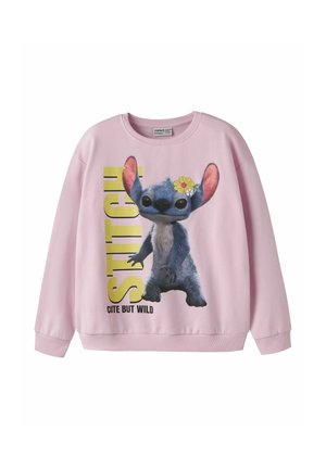 Sweat-shirt rose clair avec le personnage Stitch avec une fleur jaune à l'oreille, grand texte jaune et la phrase "Cute but wild."