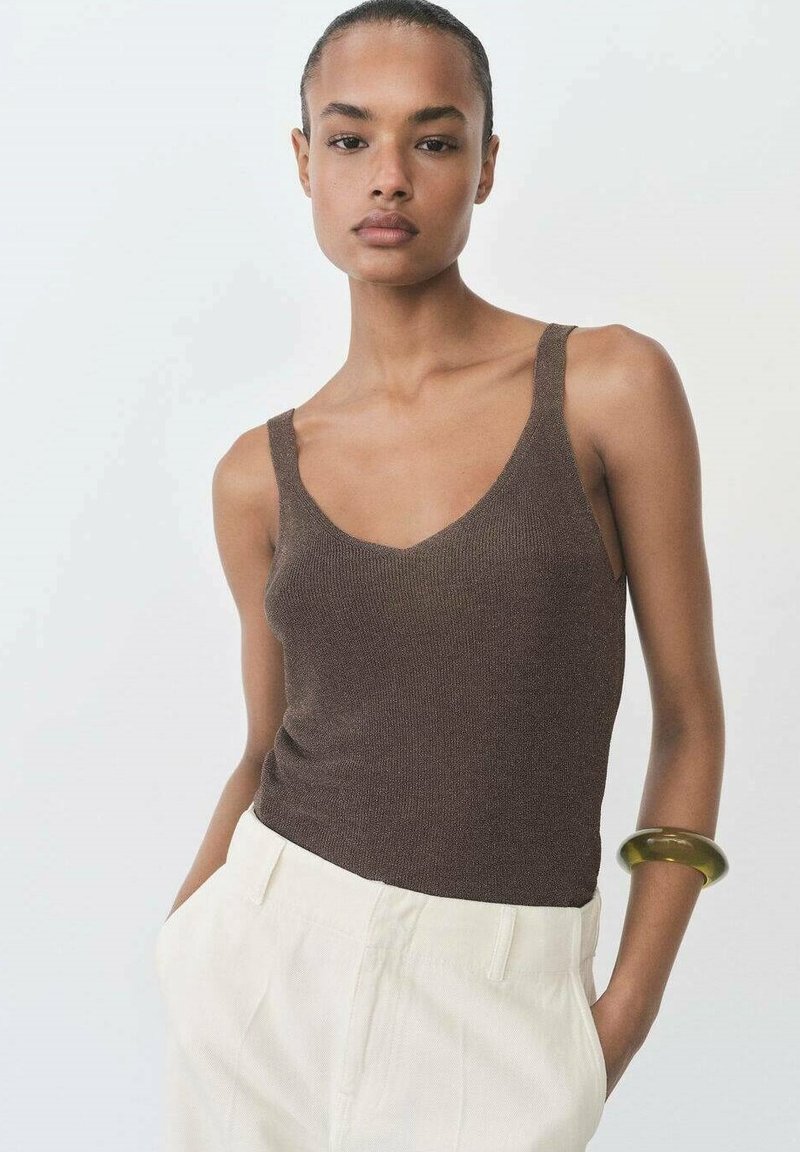 Brown ribbed tank top with a v-neckline and wide straps, paired with cream-colored high-waisted pants and a chunky bracelet.