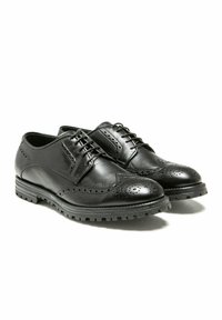 Chaussures brogue en cuir noir avec une finition lisse, un bout pointu et des perforations décoratives, dotées d'une semelle en caoutchouc ribbée robuste.