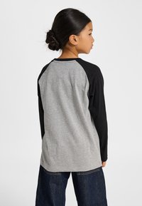 Grå och svart långärmad tröja med raglanärm, mjuk bomullstextur och kontrasterande ärmar. Sedd bakifrån.