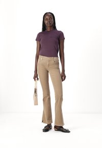 Purple fitted t-shirt, beige flared pants, black sandals, holding a light-colored handbag. Smooth fabric, casual design, minimal hardware.