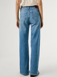 Ljust blå denimjeans med vida ben, med två bakfickor och en brun läderlapp på midjan. Slät textur.