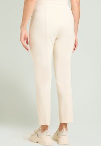 Beige slim-fit broek met een elastische tailleband, getailleerde naden en een gladde textuur, gecombineerd met lichtgekleurde sportieve sneakers.