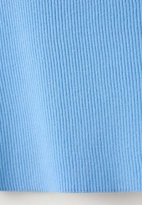 Gros plan d'un tissu côtelé bleu clair avec une texture tricotée verticale, montrant des lignes fines et régulièrement espacées en relief.