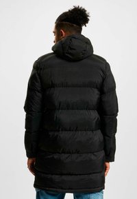 Geacă puf neagră cu glugă, design matlasat orizontal și mâneci lungi. Fabricată dintr-un material neted și lucios, cu o croială lejeră.