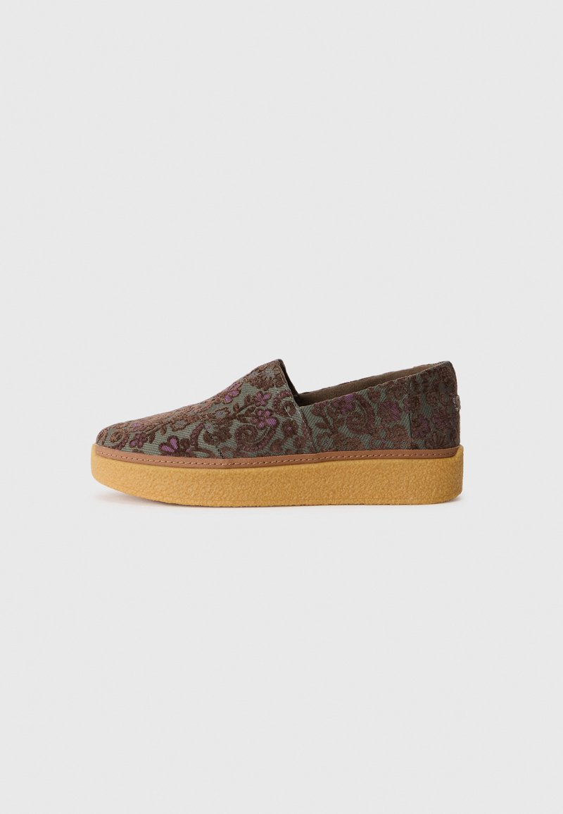 Zapatos deslizables de tela con un patrón floral en verde, marrón y morado, con un upper texturizado y una suela de goma gruesa y marrón claro.