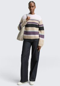 Pull en tricot multicolore avec des rayures horizontales beige, noir, violet et bleu. Associé à un jean foncé et des baskets blanches.