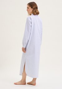Camicia da notte lunga a righe con colletto, realizzata in tessuto leggero, con maniche lunghe e uno spacco laterale per facilitare i movimenti.