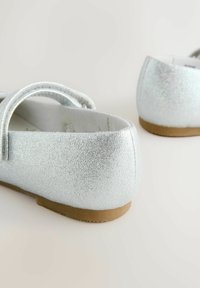 Silver ballet flats with a textured glitter finish, rounded toe, and soft soles. Features a thin strap across the instep.