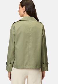 Khaki-grüne Jacke mit klassischem Kragen, Knopfakzenten und aufgerollten Ärmeln. Glatte Textur mit taillierter Passform und einfarbigem Design.