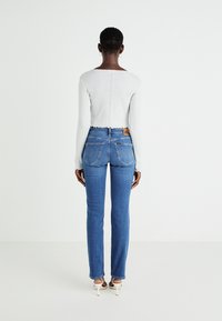 Vaaleanharmaa ribberöity pitkähiha toppi, jossa on halkopääntie, yhdistettynä sinisiin farkkuihin, joissa on merkki, takataskut ja suora lahje suunnittelu.