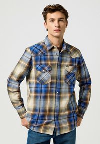 Camisa de manga larga a cuadros en azul, marrón y crema, con dos bolsillos en el pecho, yugo con puntas y diseño abotonado. Acabado de tela texturizada.