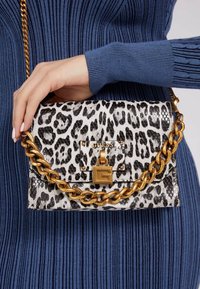 Kabelka s leopardím potiskem, zlatým řetízkovým páskem a zapínáním s logem značky. Strukturovaný design, texturovaný povrch a kontrastní barevná paleta.