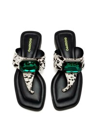 Des tongs noires avec une sangle tachetée de blanc, dotées d'un large accent en pierre précieuse verte. La semelle est texturée et a une forme carrée.